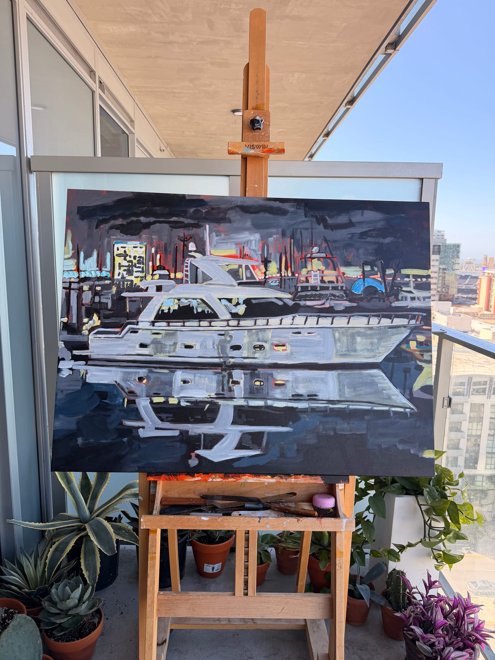 Piper's painting of a white yacht reflected in a dark harbor at night, on a wooden easel on a sunny San Diego balcony surrounded by potted succulents
